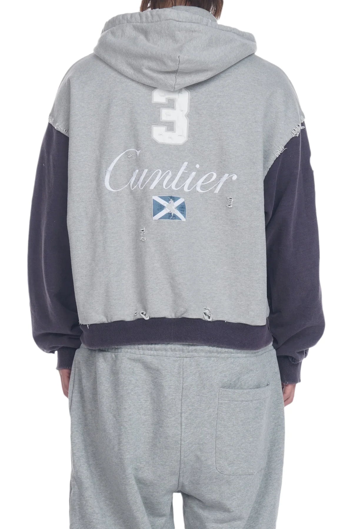 Back view of a person wearing a gray hooded sweatshirt with dark navy sleeves and a distressed hem, featuring the number 3, 'Cuntier' script, and a Scottish flag graphic on the back, paired with matching gray sweatpants.