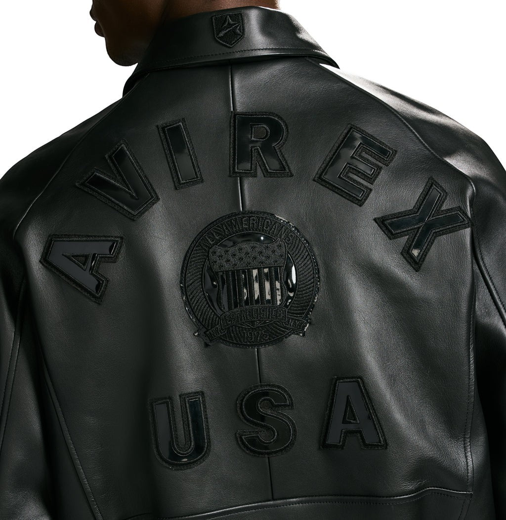 OFFCODE.USA Avirex black leather bomber jacket with logo details on collar, back, and chest. Features front zipper and ribbed hem.
